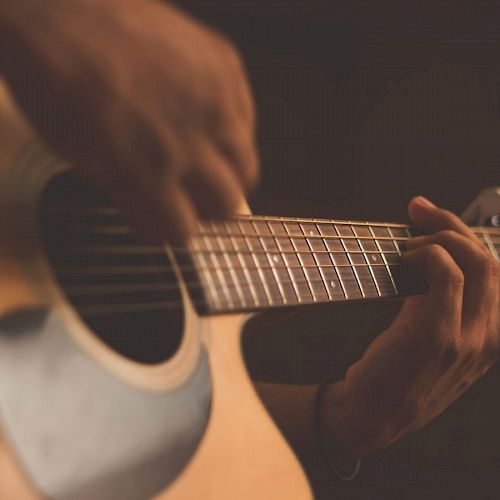 The image shows a close-up of hands playing an acoustic guitar, focusing on the neck and strings of the instrument.