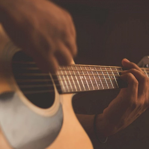 A close-up of a person playing an acoustic guitar, focusing on the hands and strings, with a dark background.